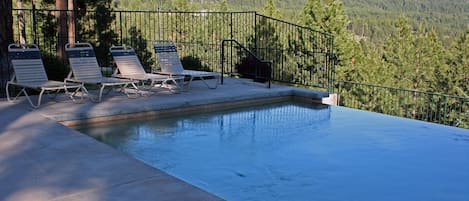 An infinity pool with lounge chairs and a view of a forested mountain range.