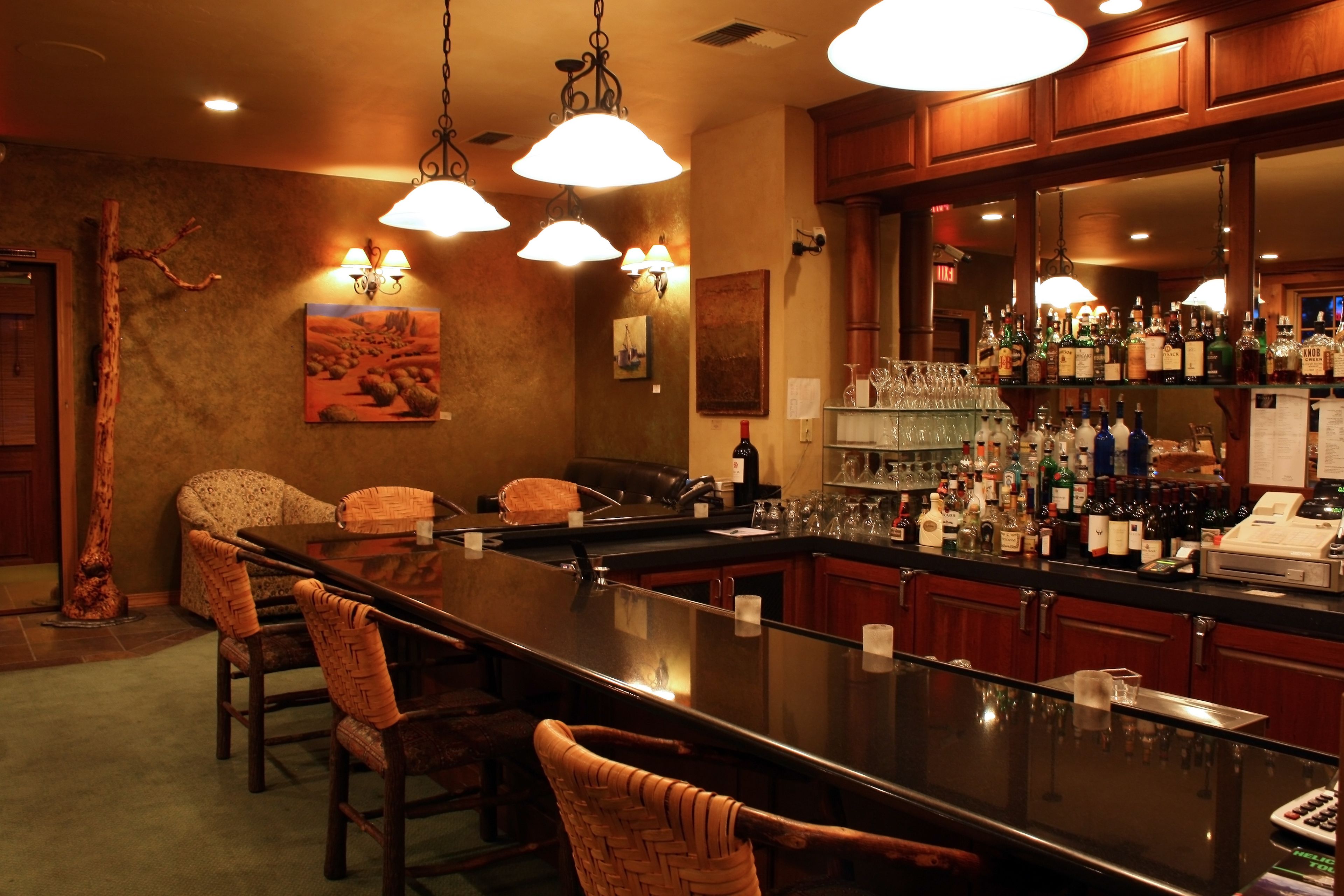 Zona de bar con una barra larga, varias sillas y una diversidad de botellas y vasos.