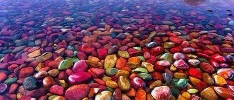 A calm lake with a reflection of mountains and a colorful pebble beach.