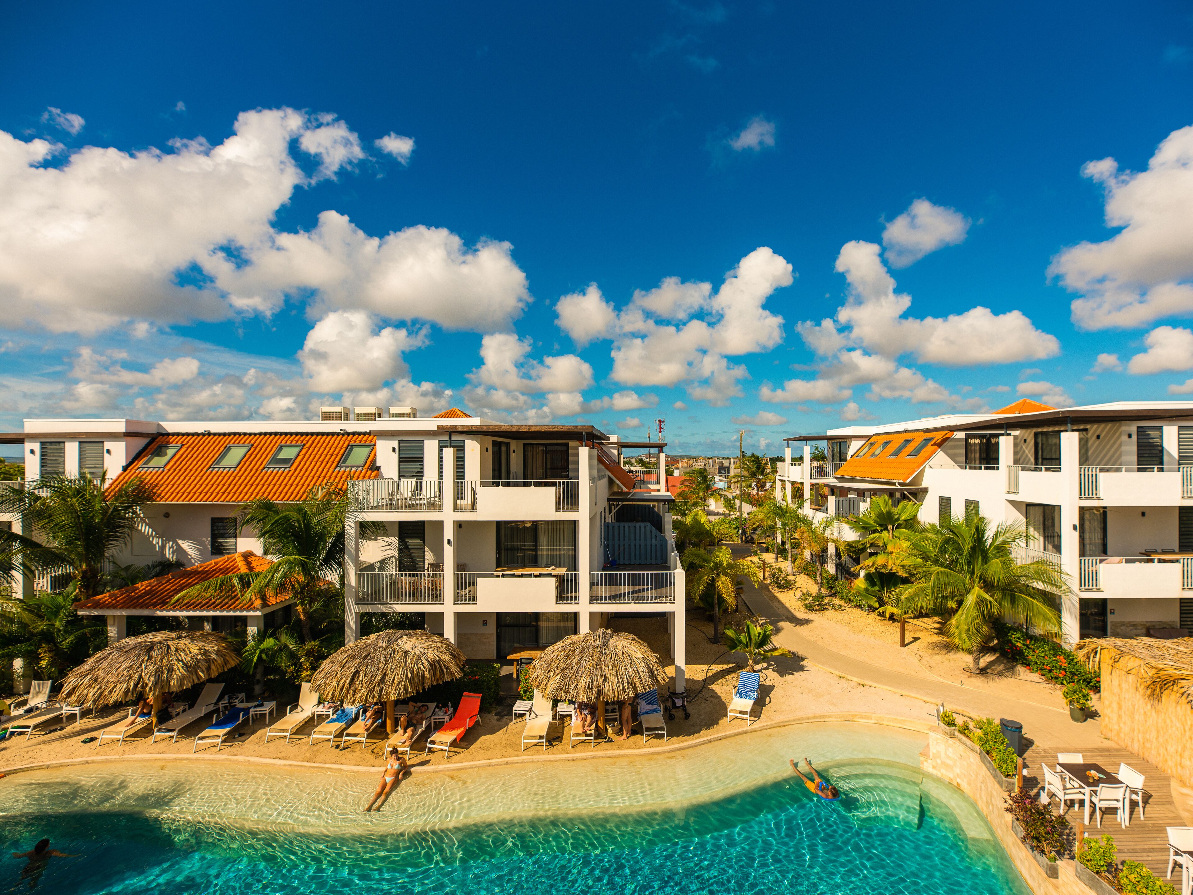 A resort with a swimming pool, sun loungers, and thatched umbrellas.