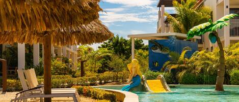 A pool area with lounge chairs, a thatched umbrella, and a mural of a turtle and mermaid.