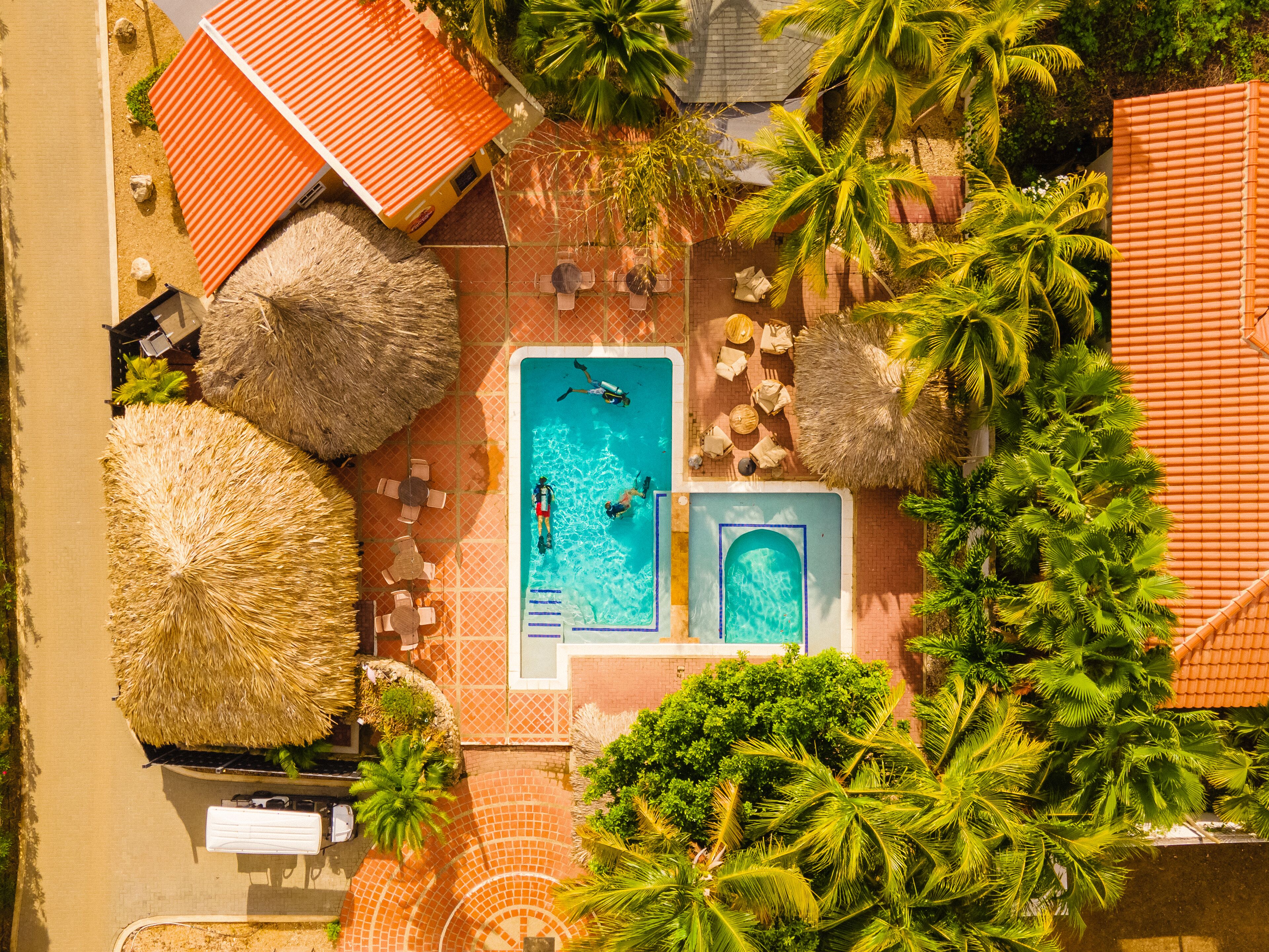 Luchtbeeld van een resort met een zwembad, palmbomen en rieten parasols.