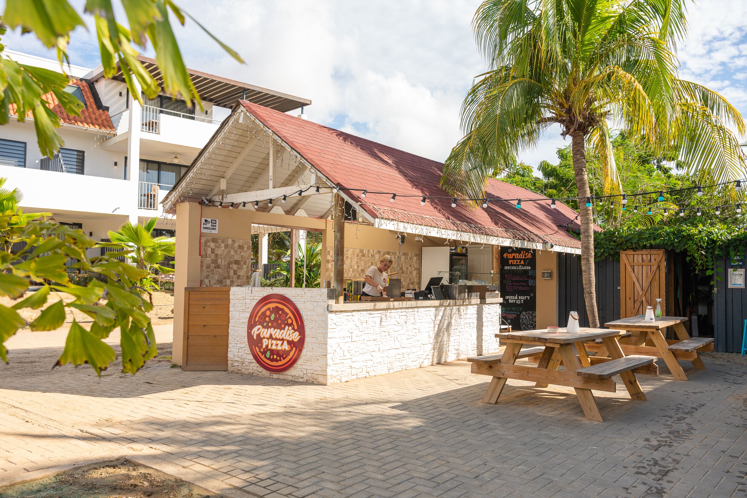 Un stand de restauration avec une enseigne indiquant « Paradise Pizza » et des tables à l’extérieur.