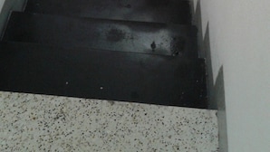 A staircase with a white wall and a black step. A small, square, cardboard box is placed on the floor next to the wall.