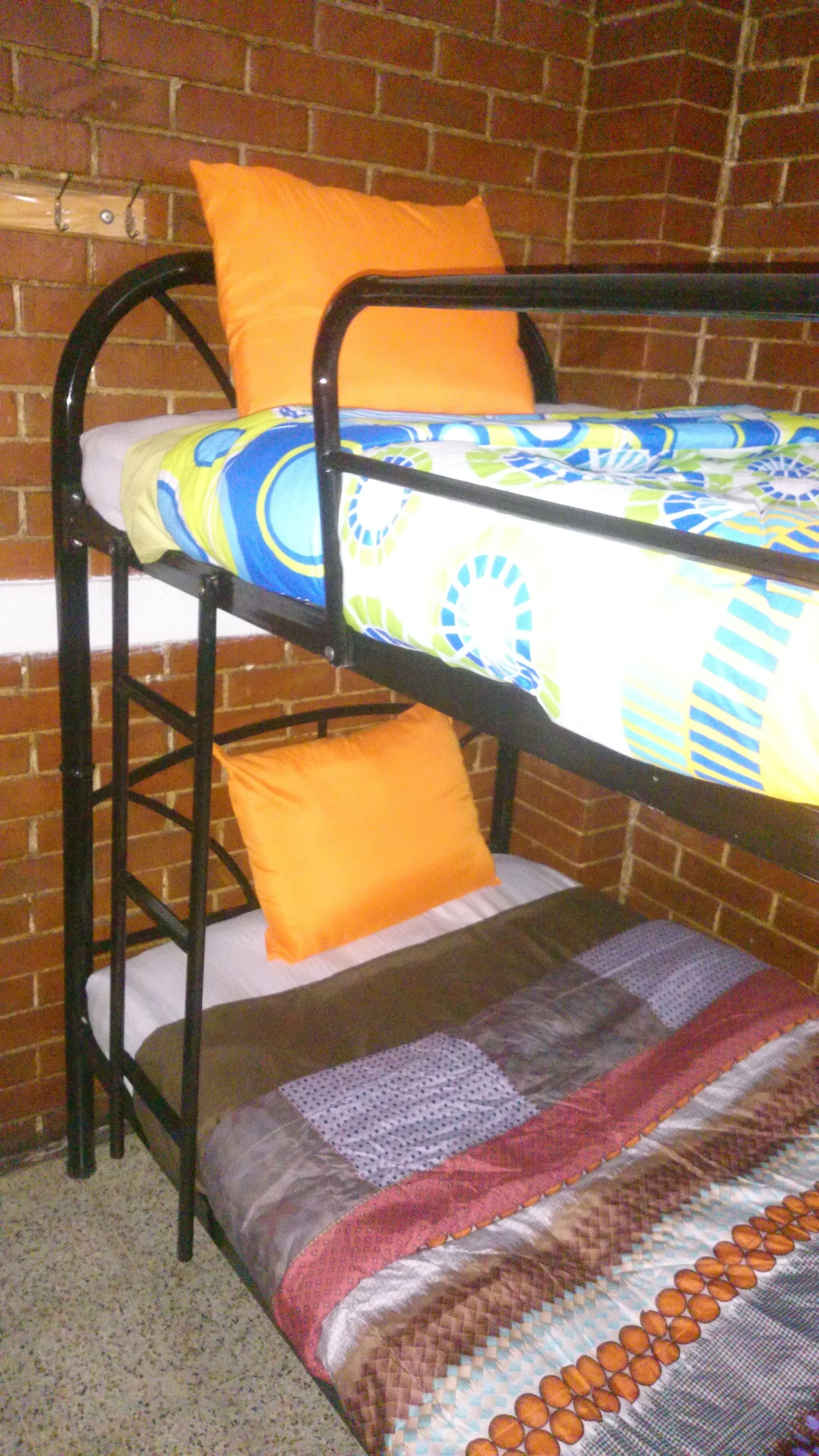 Un lit superposé avec une couvre-lit colorée et deux oreillers orange.
