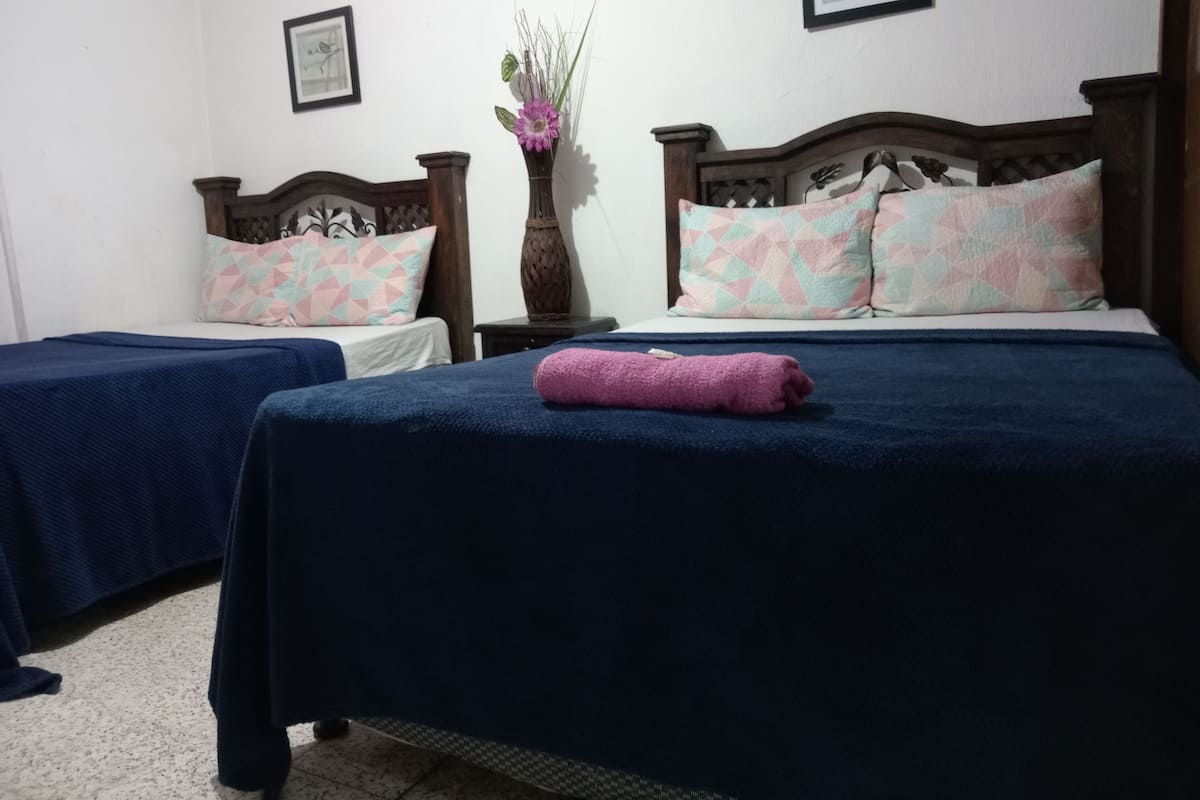 A hotel room with two beds, each with a different patterned bedspread, a nightstand with a vase, and framed pictures on the wall.