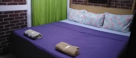 A bed with a purple bedspread, two folded towels, and patterned pillows.