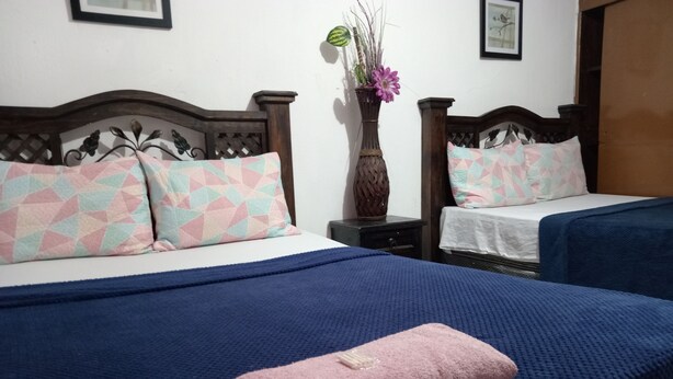 A hotel room with two beds, each with a different patterned bedspread, a nightstand with a vase of flowers, and a framed picture on the wall.