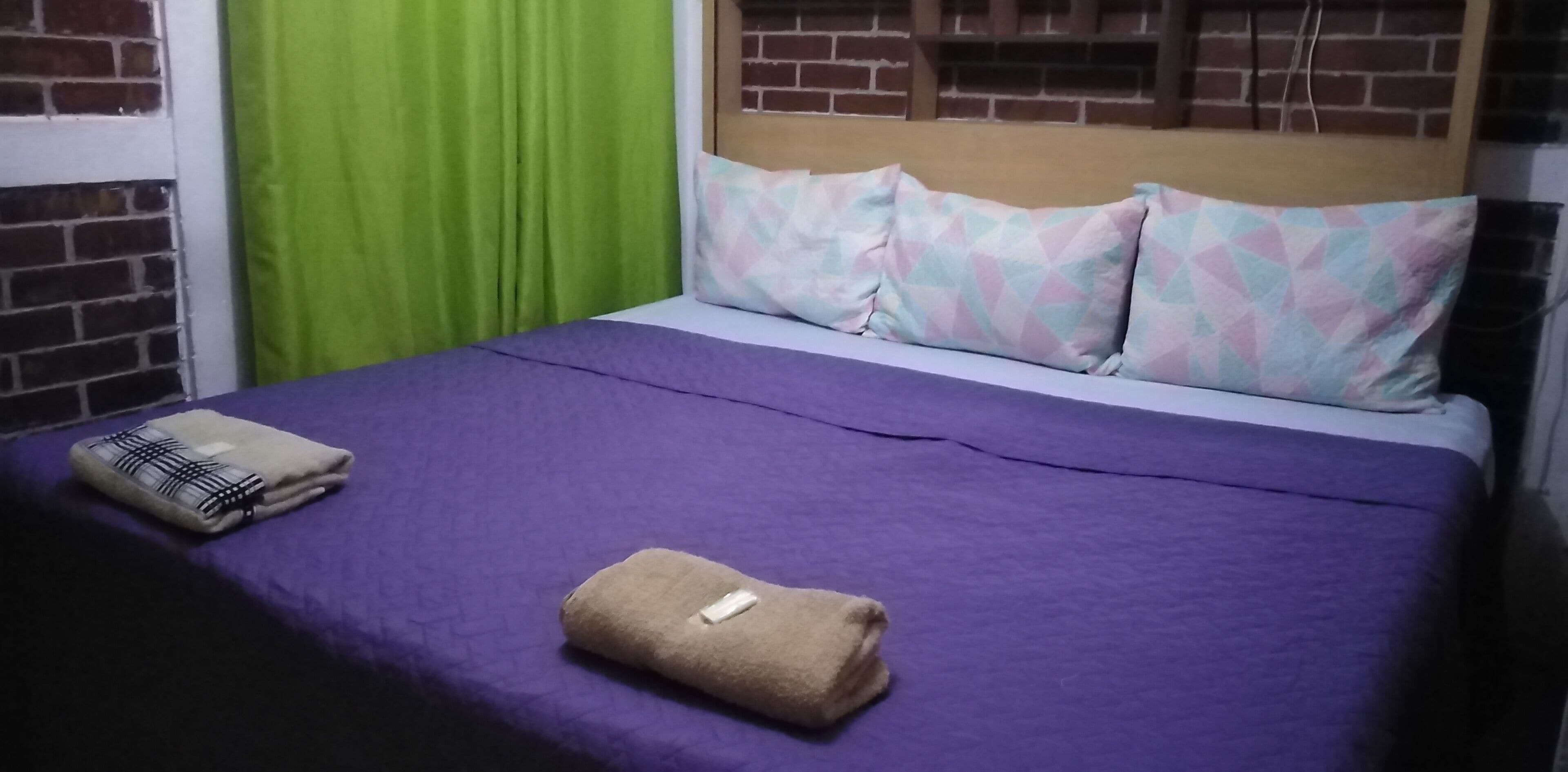 A bed with a purple bedspread, two pillows, and two folded towels.