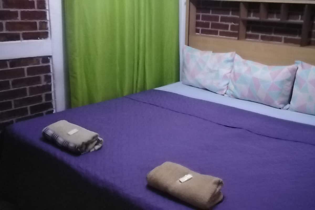 A bed with a purple bedspread, two pillows, and two folded towels.
