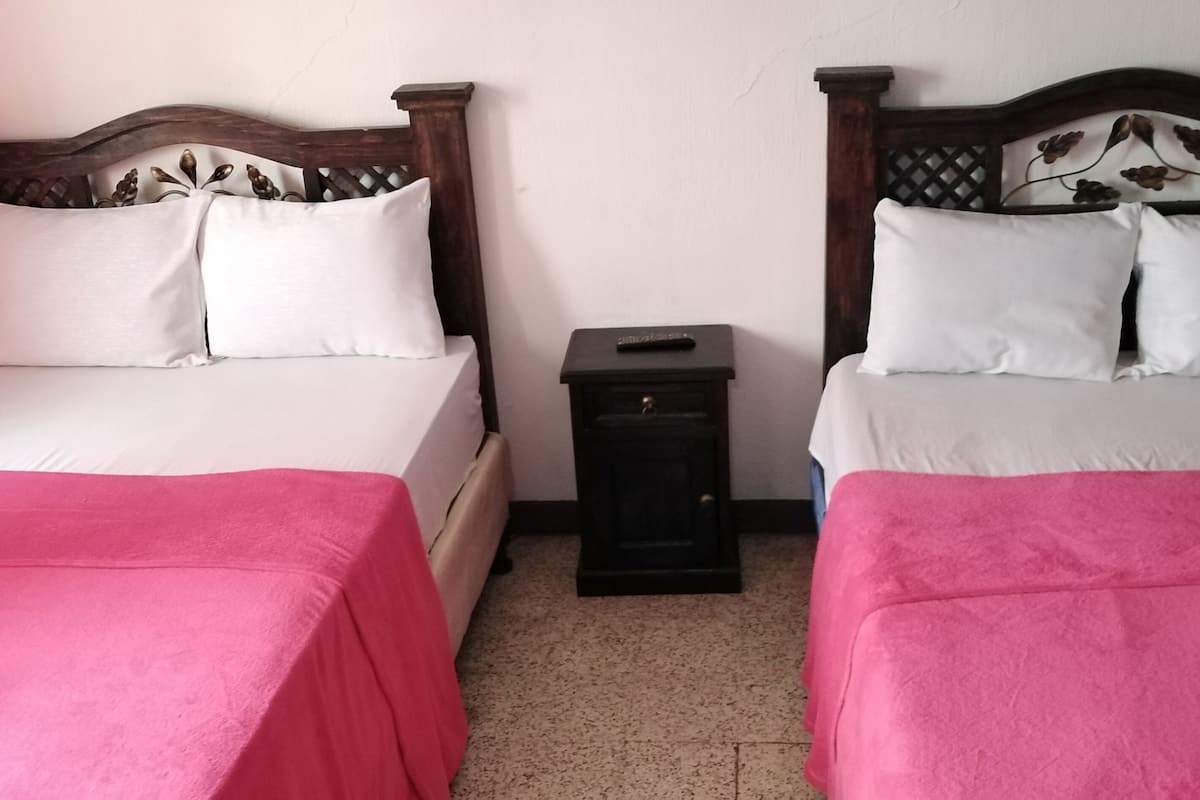 Two single beds with wooden headboards, white and pink bedding, and a small bedside table with a remote control.