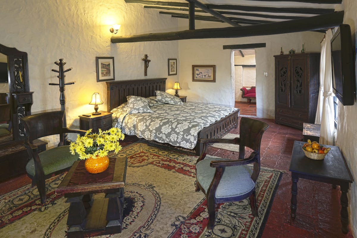 Una habitación tradicional con cama, muebles de madera, una mesa con un jarrón de flores y un televisor en la pared.