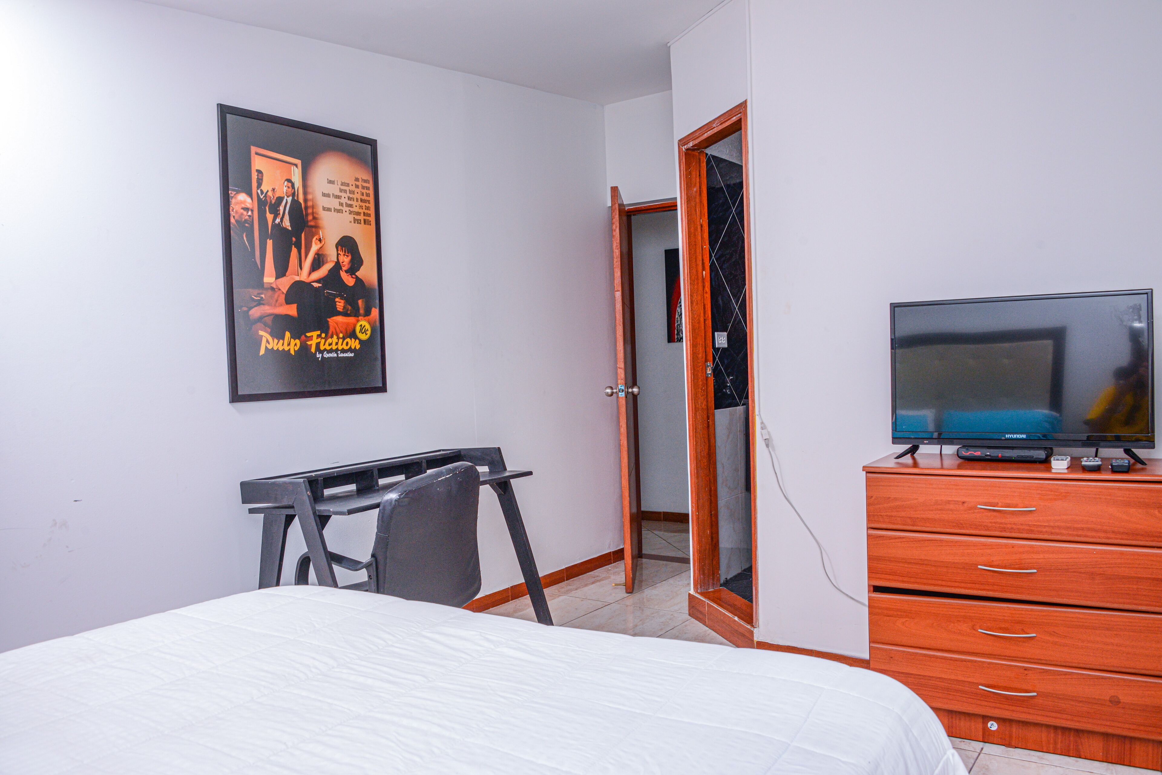 A bedroom with a bed, a desk, a dresser, a television, and a poster on the wall.