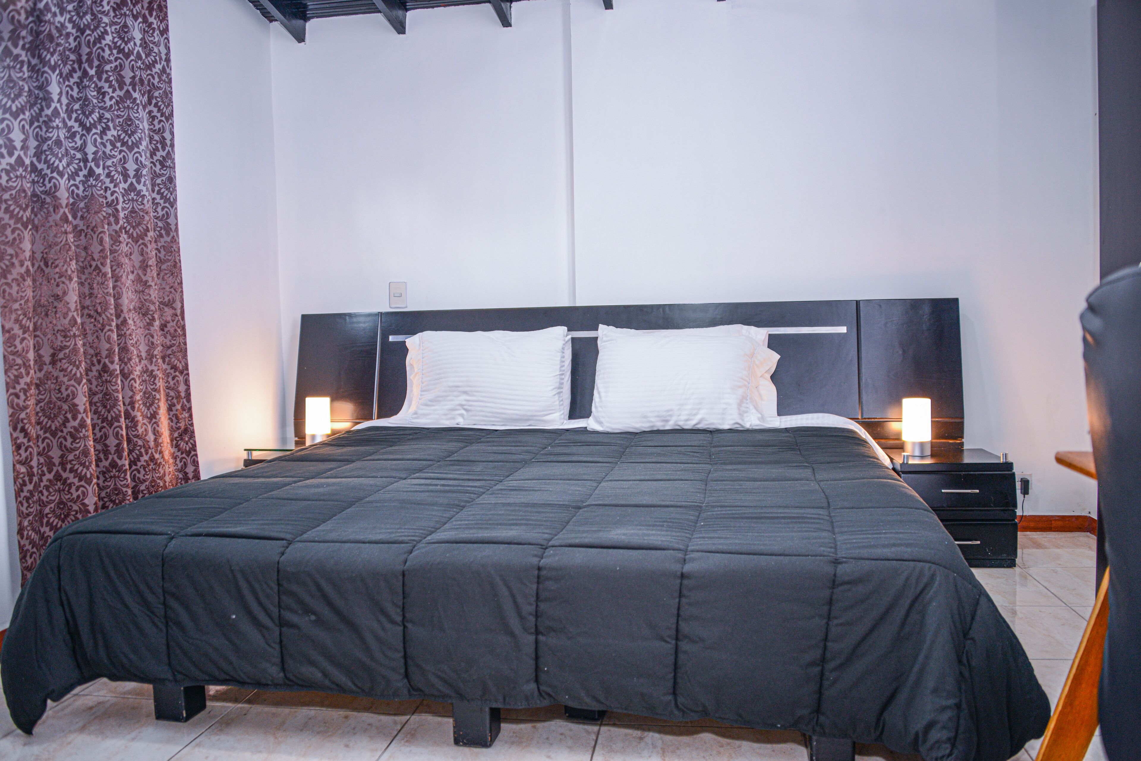 Een moderne slaapkamer met een groot bed, twee nachtkastjes met lampen en behang met patroon.