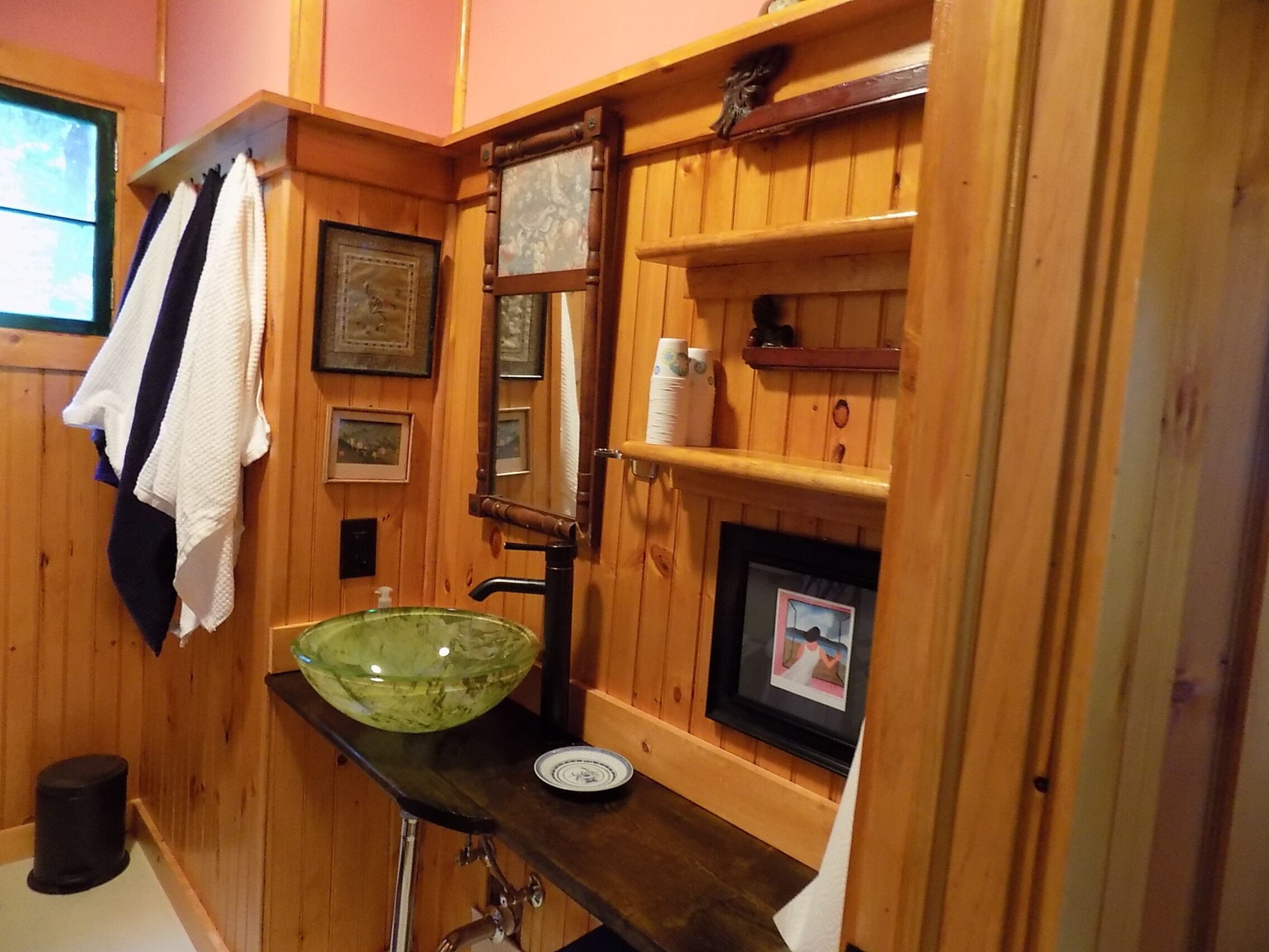 Un bagno in legno con un lavabo in vetro verde, quadri appesi e asciugamani appesi al muro.