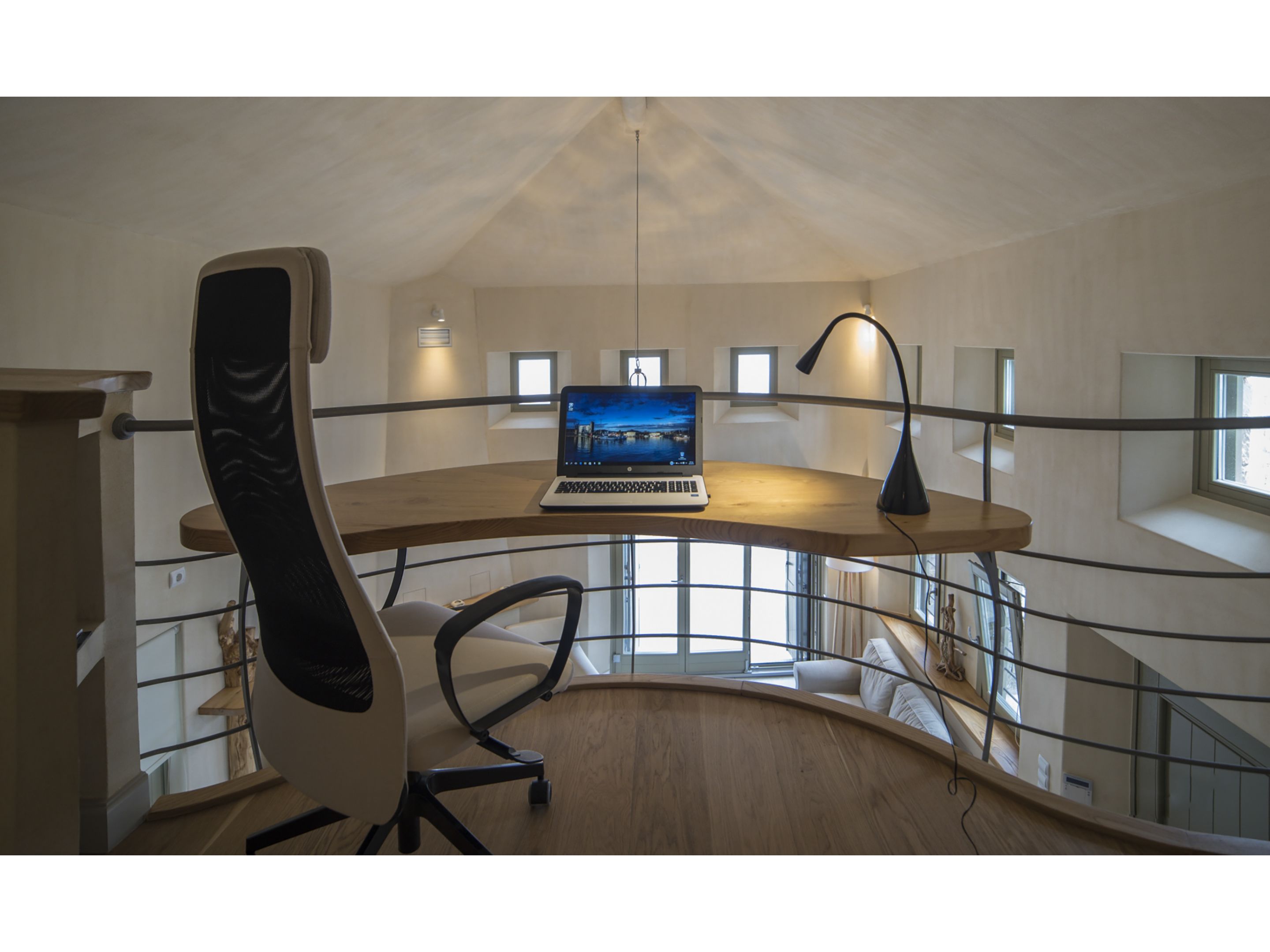 Ein modernes Loft-Zimmer mit einem gewölbten Schreibtisch, einem Laptop und einem Hochstuhl.