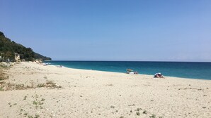Una playa con cielo despejado, orilla arenosa y algunas personas.