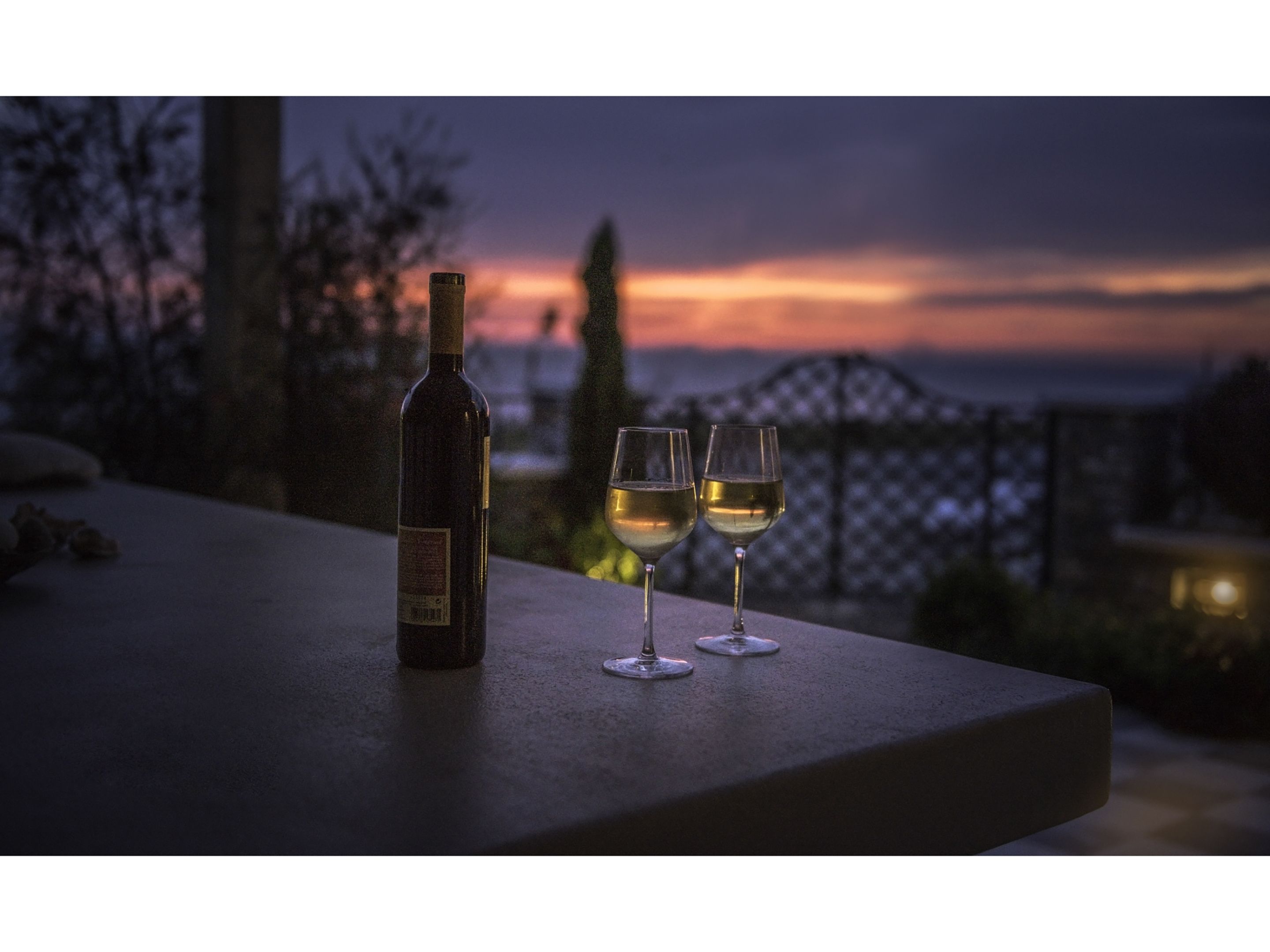 A bottle of wine and two glasses on a table with a view of a sunset.