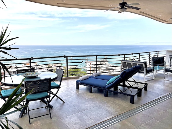 Ein Balkon mit Tisch und Stühlen, einem Liegestuhl und Blick auf den Ozean.