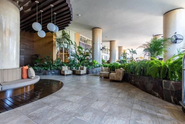 A spacious lobby with a curved seating area, large pillars, and a variety of plants.