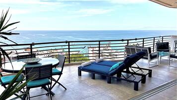 Un balcon avec une table et des chaises, un fauteuil de relaxation et une vue sur l’océan.