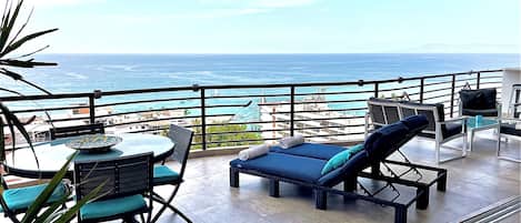 Een balkon met een tafel en stoelen, een lounge stoel en uitzicht op de oceaan.