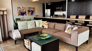 A modern living room with a sectional sofa, a coffee table, and a kitchen area in the background. - Signature 406 Private Pool Sept 18-23 @ -50%, Oct 18-23 @ -40%, Nov 18-22 @ -25% (Puerto Vallarta,)