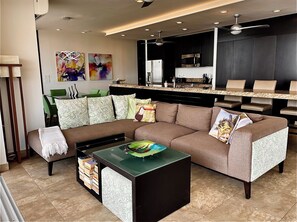 A modern living room with a sectional sofa, a coffee table, and a kitchen area in the background.