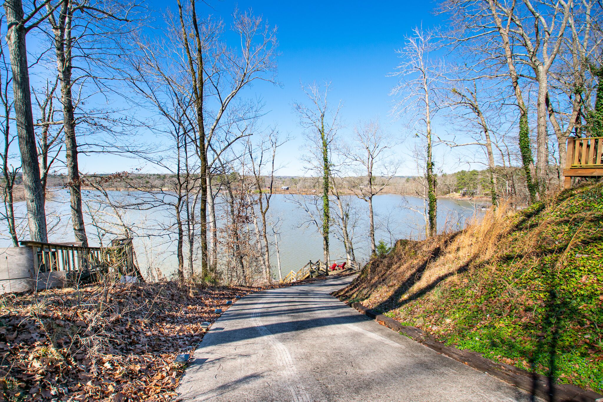 A paved road leading to a body of water, surrounded by leafless trees and a wooden structure on the right.