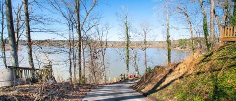 A paved road leading to a body of water, surrounded by leafless trees and a wooden structure on the right.