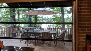Un patio al aire libre con una mesa y sillas, un parasol grande y vistas a árboles a través de un ventanal.