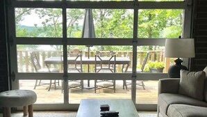 Habitación con un amplio ventanal corredero que da a un patio exterior. En el interior, hay una mesa de madera con un mando a distancia, un banco acolchado y un sofá.