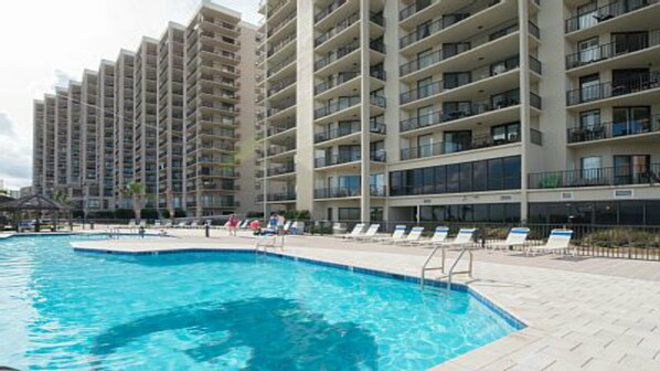 A swimming pool with lounge chairs and a high-rise building in the background. - Walkout to beach, pool and splashpad 3 bedroom 2 bath ground floor condo. (Orange Beach)