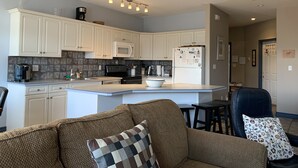 A modern kitchen with white cabinets, a microwave, a refrigerator, and a coffee maker. There is a brown couch with a checkered pillow and a floral pillow. - Fairmont Hot Springs Get-A-Way - Escape with Ease (Fairmont Hot Springs)