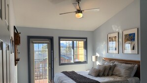 A bedroom with a bed, a ceiling fan, two windows, and framed pictures on the wall. - Fairmont Hot Springs Get-A-Way - Escape with Ease (Fairmont Hot Springs)