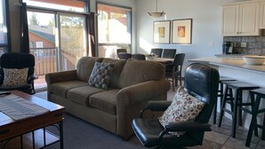 A living room with a sofa, a dining table, and chairs. There is a kitchen area with cabinets and a countertop. - Fairmont Hot Springs Get-A-Way - Escape with Ease (Fairmont Hot Springs)