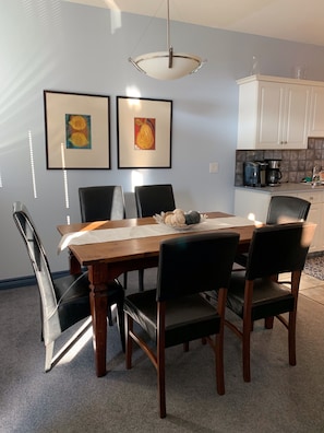 A dining area with a wooden table and chairs, a chandelier, and two framed artworks on the wall.