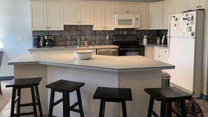 A kitchen with white cabinets, a microwave, stove, and a refrigerator. There are three black stools at the island. - Fairmont Hot Springs Get-A-Way - Escape with Ease (Fairmont Hot Springs)