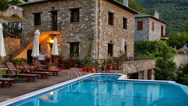 Un edificio in pietra con piscina, area salotto esterna e vista sulle colline circostanti.