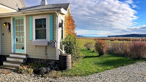 A quaint house with a front porch, a chimney, and a view of a grassy field. - Classic Maine Oceanfront Cottage, Gorgeous Views, Centrally Located, Pets, A/C (Lubec)