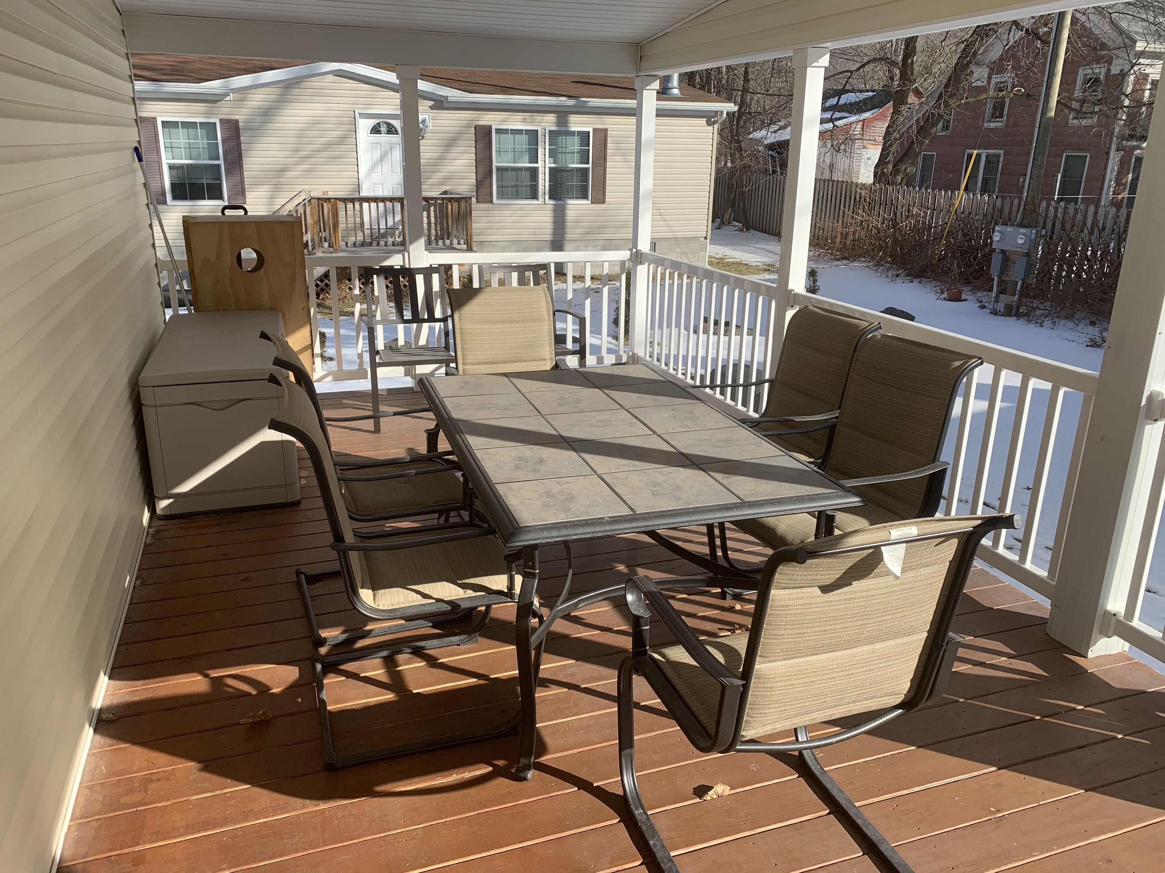 A covered patio with a table and chairs, a small refrigerator, and a view of a house in the background.