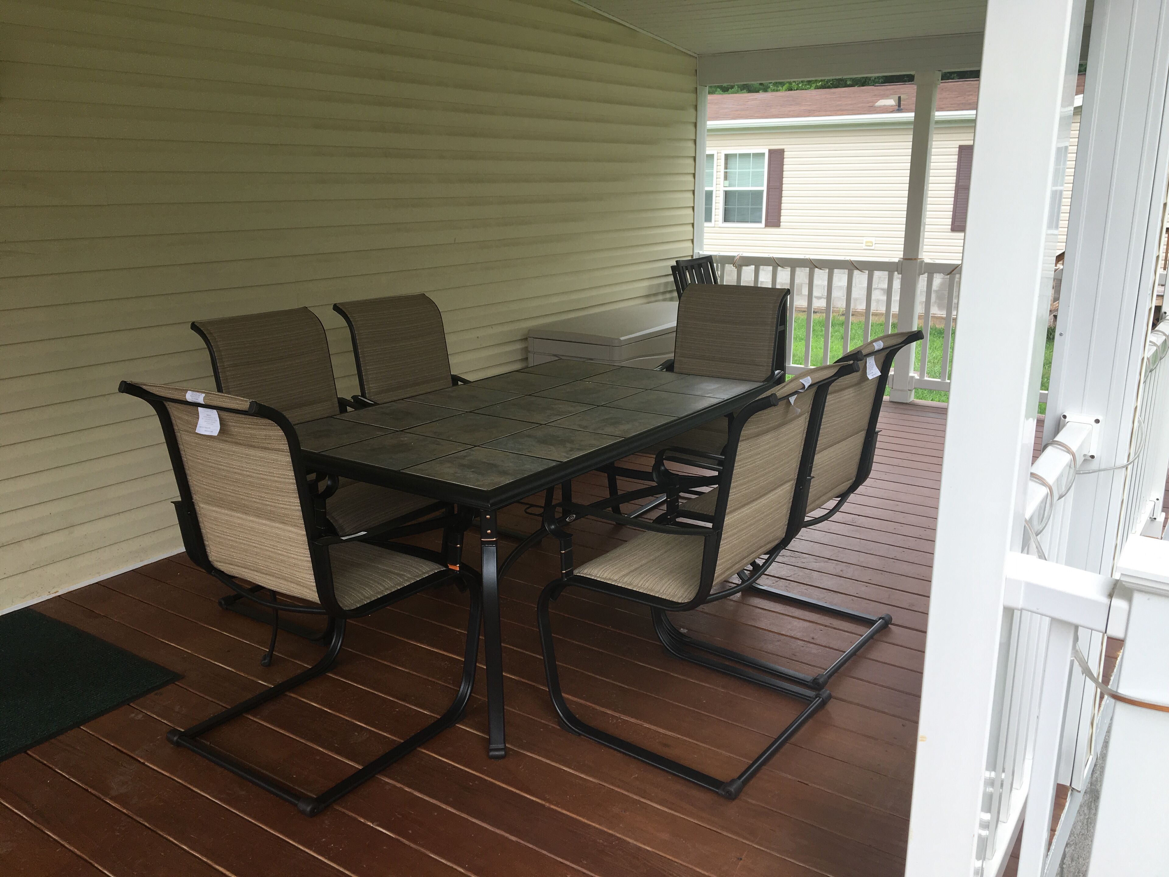 Eine überdachte Terrasse mit einem rechteckigen Tisch und vier Stühlen, mit Metallgestell und geflochtenen Sitzkissen.