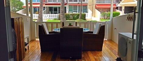An outdoor patio with a wooden deck, a round table with chairs, and a white fence.