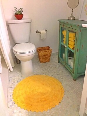 Ein Badezimmer mit Toilette, einem Korb, einer gelben Matte und einem Schrank mit Handtüchern.