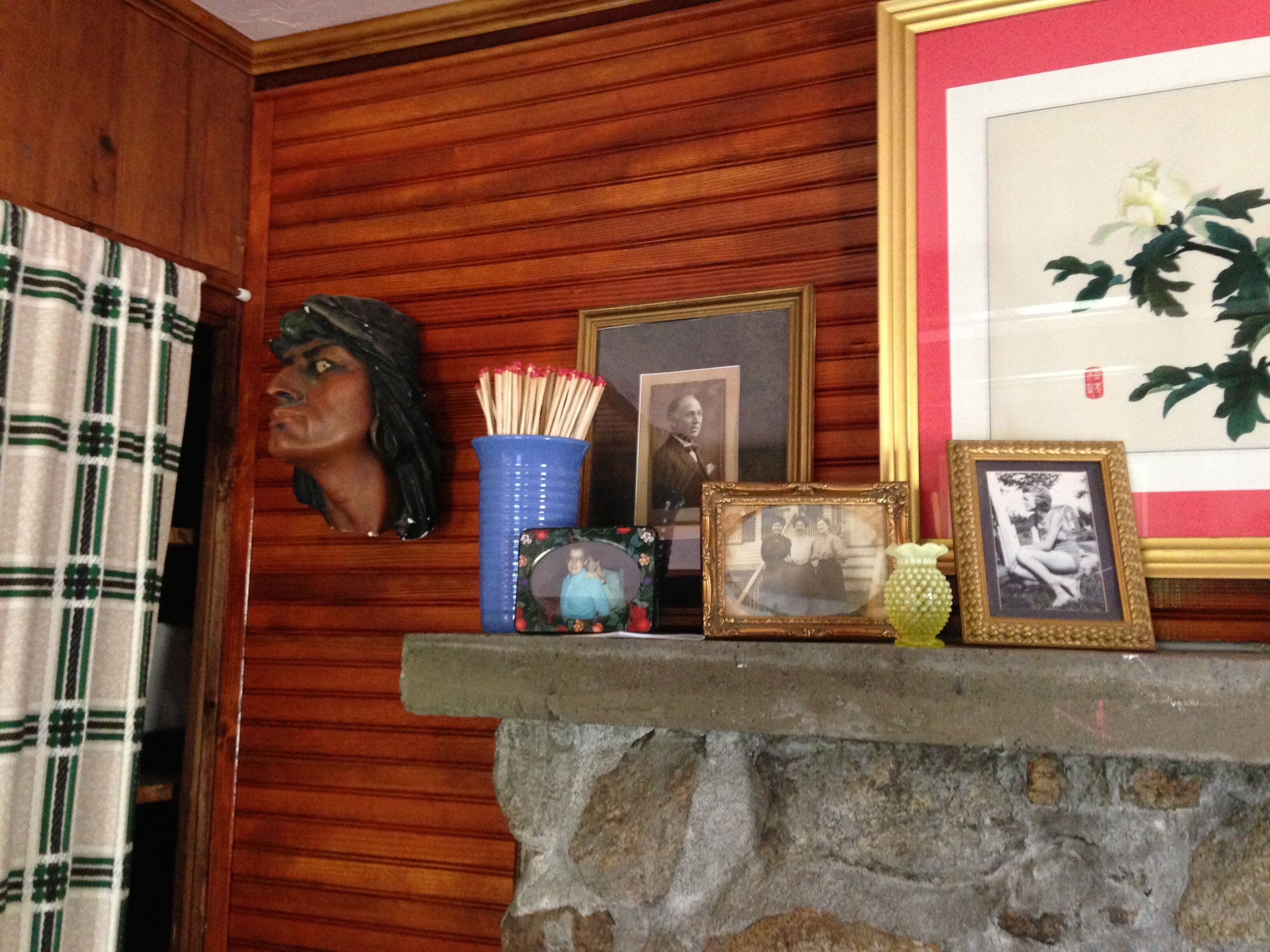 A stone fireplace with a shelf displaying framed photographs, a globe, and a vase with a plant.