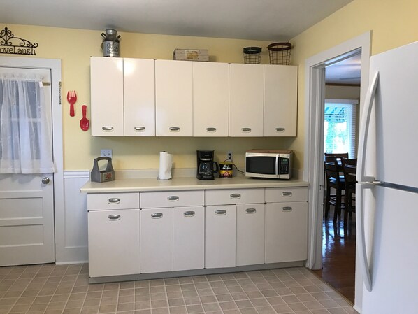 Una cocina con armarios blancos, microondas y cafetera.