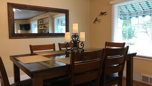 Un comedor con una mesa de madera, sillas, un espejo y una ventana con persianas.