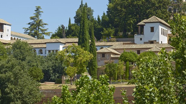 Un edificio tradizionale con diversi archi e un campanile, circondato da vegetazione lussureggiante e alberi.