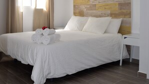 Un lit bien fait, avec des serviettes pliées et un sommier décoratif, une table de chevet et une fenêtre avec des rideaux.