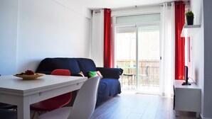 Un salon moderne avec une table à manger blanche, des chaises rouges et blanches, un canapé bleu et un petit meuble blanc.
